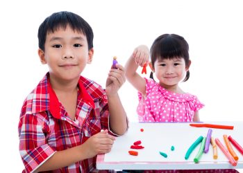 Little asian children playing and creating toys from play dough on table. Boy and girl smiling and show works from clay at camera, over white background. Strengthen the imagination of child